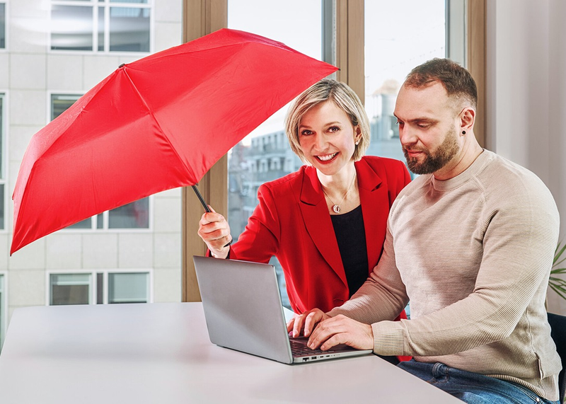 Zwei Personen arbeiten gemeinsam an einem Laptop, rote Schutzschirm-Symbolik