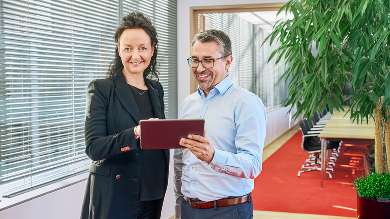 Zwei Personen betrachten ein Tablet in einem modernen Büro