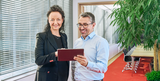 Zwei Personen betrachten ein Tablet in einem modernen Büro