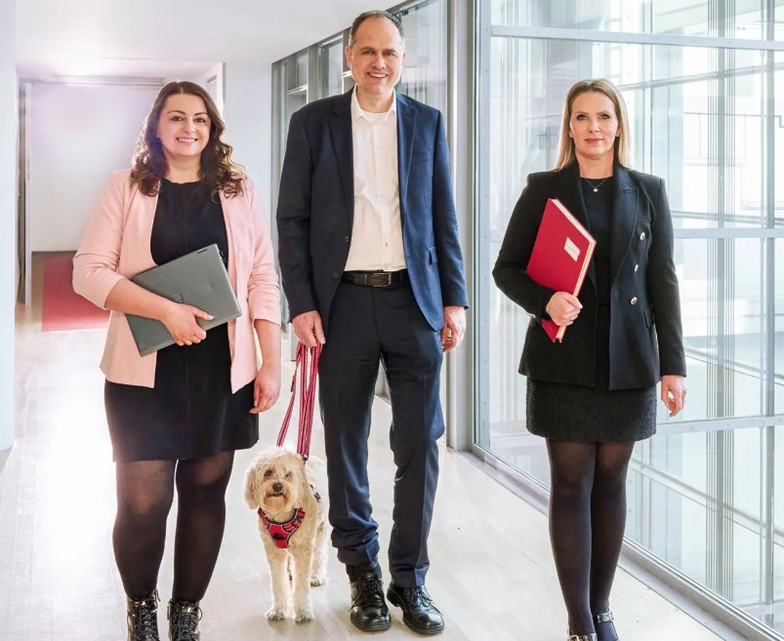 Drei Personen gehen durch ein Bürogebäude mit Unterlagen