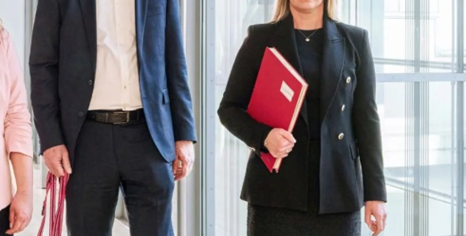 Drei Personen gehen durch ein Bürogebäude mit Unterlagen